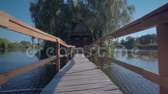 阳光明媚的一天一座长长的木桥通向河对岸的一座木屋视频的预览图