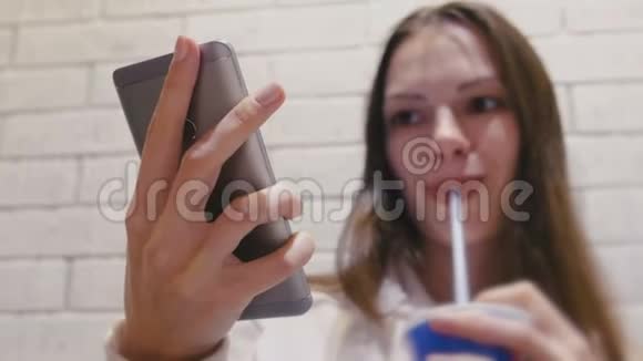 微笑着的美女正在喝着一杯管子里的饮料在咖啡馆里用手机看视频视频的预览图
