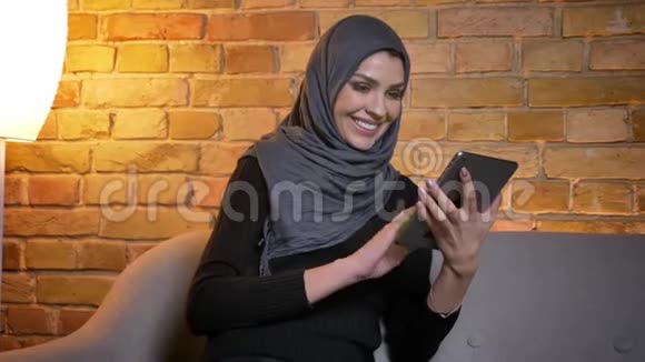 用平板电脑拍摄成年穆斯林女性戴头巾的特写肖像并在镜头中显示绿色彩色屏幕视频的预览图