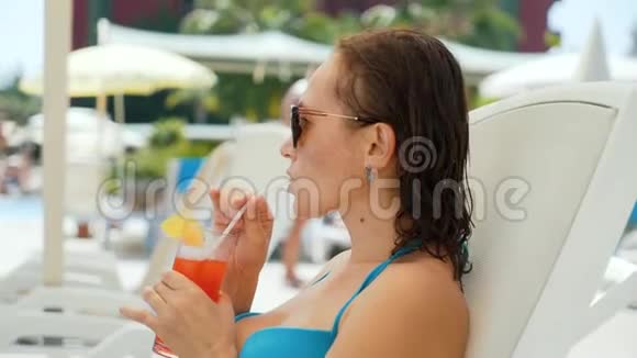 女人一边喝鸡尾酒一边坐在游泳池附近的休息室里视频的预览图