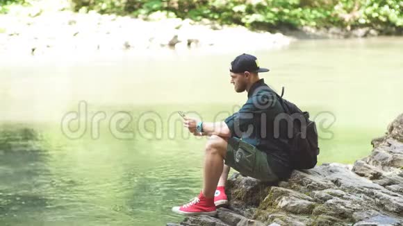 一个带背包的游客坐在一个狂野的夏天的树林里远征视频的预览图