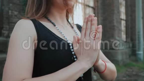 穿着黑色紧身衣的年轻女孩正在一座废弃的大楼附近用namastemudra练习瑜伽里面有一个大窗户视频的预览图