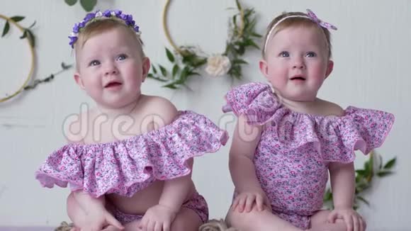 穿粉色衣服的女双胞胎在墙上的背景上摆着装饰的照片视频的预览图