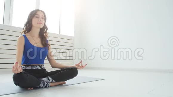 运动的年轻女性练习瑜伽坐在半莲花锻炼Siddhasana姿势室内家庭内部背景视频的预览图