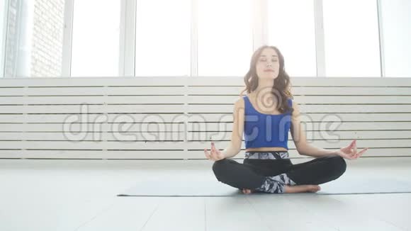 运动的年轻女性练习瑜伽坐在半莲花锻炼Siddhasana姿势室内家庭内部背景视频的预览图