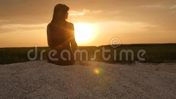坐在沙滩上欣赏日落的女孩剪影与自然和谐的美丽女人的身影概念暑假特拉视频的预览图