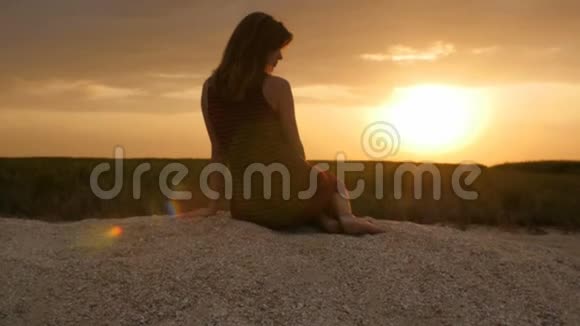 坐在沙滩上欣赏日落的女孩剪影与自然和谐的美丽女人的身影概念暑假特拉视频的预览图