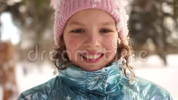 微笑的女孩在公园里享受寒冷阳光的早晨一个在雪地里玩耍的女学生的肖像画粉色视频的预览图