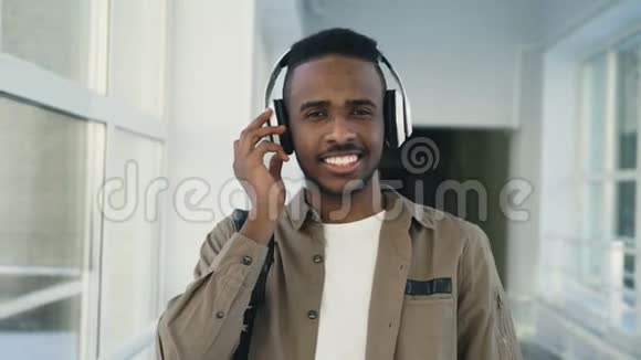 年轻英俊的非洲学生戴着大耳机站在宽阔的白色大学走廊上跳舞的肖像视频的预览图