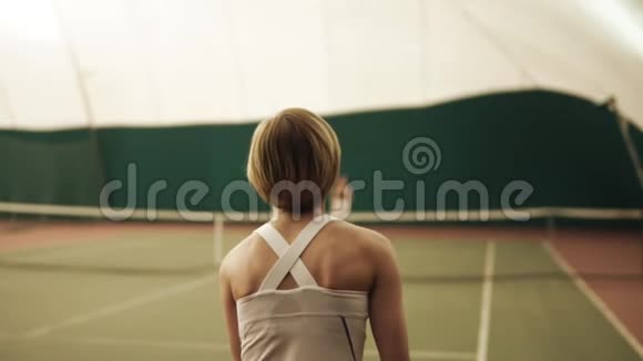 一名活跃的女网球运动员在网球场用球拍击球的背面镜头室内运动慢动作视频的预览图