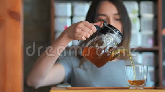 年轻的微笑的女人从玻璃水壶里往杯子里倒红茶视频的预览图