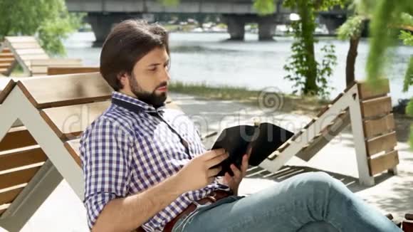 他坐在长凳上看书然后他在电话里得到消息有人拿着它看着电话视频的预览图