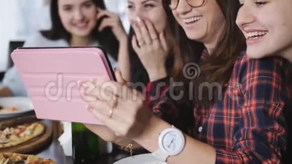 四个快乐的女朋友在一家餐馆吃披萨喝啤酒看平板电脑上的照片视频的预览图