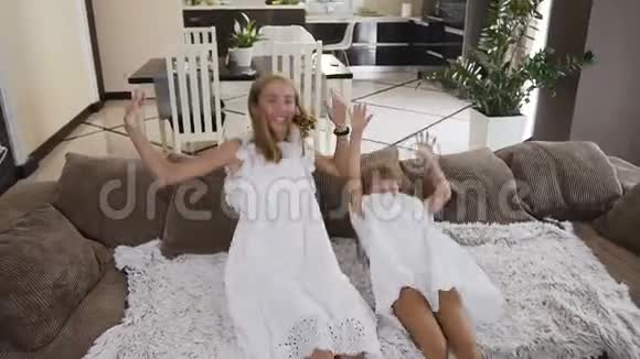 迷人的两个女孩有趣地摔倒躺在沙发上张开双臂在他们家的客厅里的概念视频的预览图