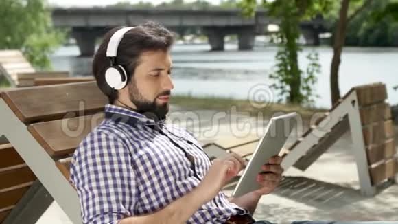 他躺在长凳上通过耳机听音乐他还拿着平板电脑在屏幕上打字人类是视频的预览图