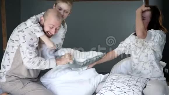 睡衣派对儿子和父母穿着相同的睡衣在床上用枕头打对方视频的预览图