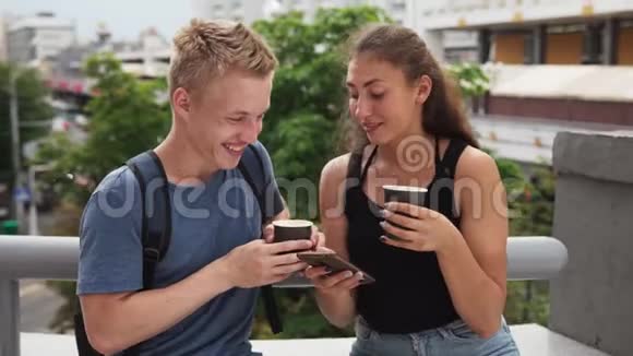 年轻的幸福夫妇在城市大街喝咖啡使用智能手机视频的预览图
