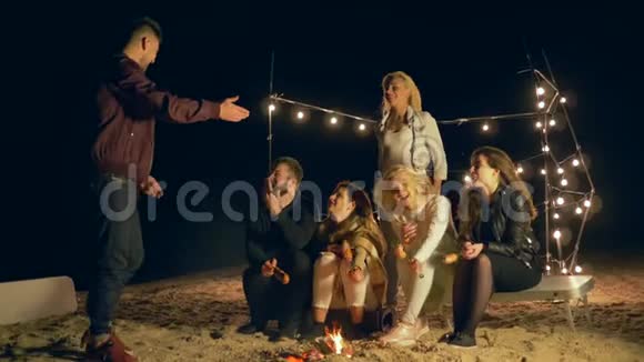 海滩娱乐朋友们在晚上野餐时坐在篝火旁玩有趣的游戏视频的预览图