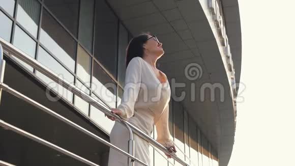 年轻的白种人商务女性抓住栏杆在日落时眺望城市布鲁内特女孩享受日落和温暖视频的预览图