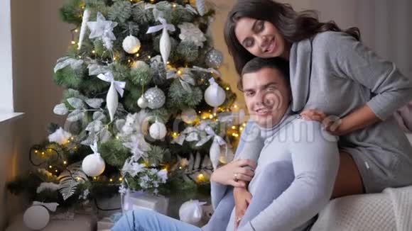 甜蜜的时刻女孩拥抱丈夫在家圣诞前夕看着镜头靠近杉树视频的预览图