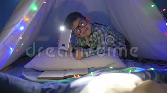 学龄前家庭教育小男孩戴眼镜晚上在wigwam用手机看书视频的预览图