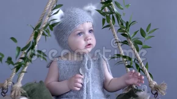 穿着老鼠服装的孩子坐在悬挂的秋千上蓝色背景上装饰着绿叶视频的预览图