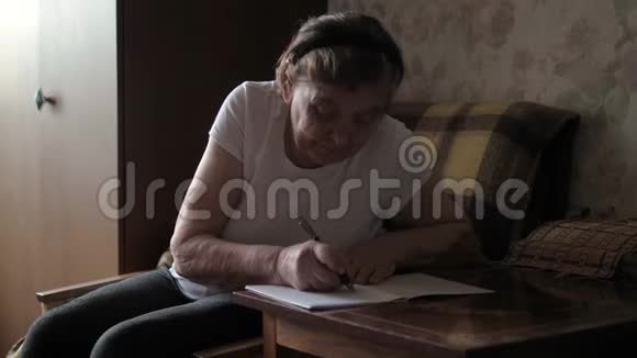 一位年老的老妇人坐在桌旁用纸写信息视频的预览图
