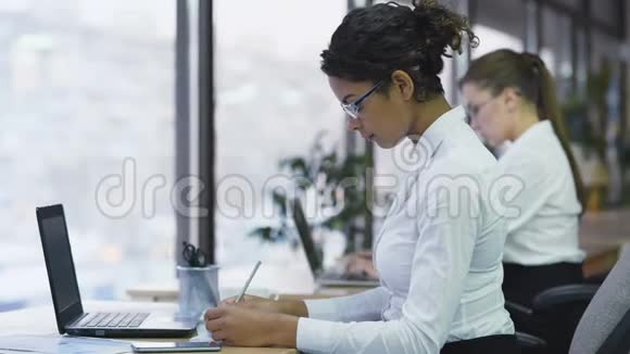 混合种族商业女性做笔记在笔记本电脑上打字勤奋的经理视频的预览图