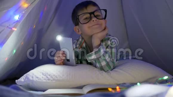 戴眼镜的男孩梦中的肖像手里拿着电话躺在帐篷里视频的预览图