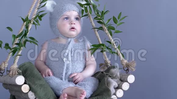 孩子们的时光穿着小猫服装的大眼睛坐在木制秋千上蓝色背景上有绿色的树枝视频的预览图