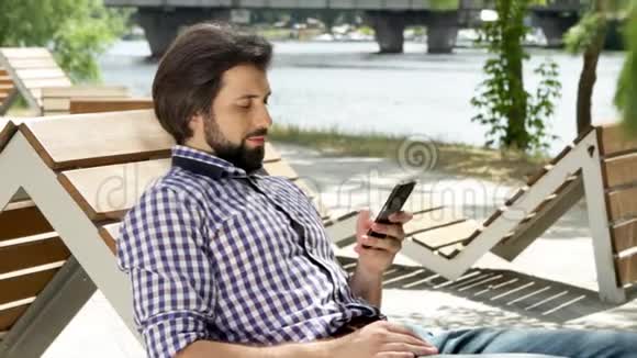 男人躺在长凳上拿着电话他正在看它并输入信息他在笑然后他就把视频的预览图
