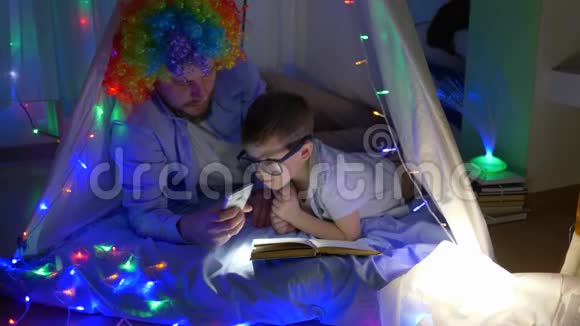 孩子们的童话故事留胡子的男人和儿子一起戴上小丑假发在帐篷里用花环打开手电筒视频的预览图