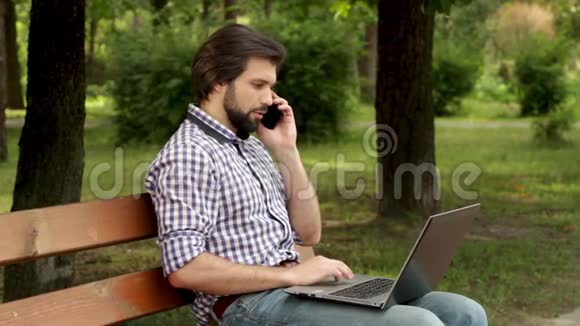 忙碌的人正坐在长凳上用笔记本电脑工作他正在打字他在打电话他拿的离左边很近视频的预览图