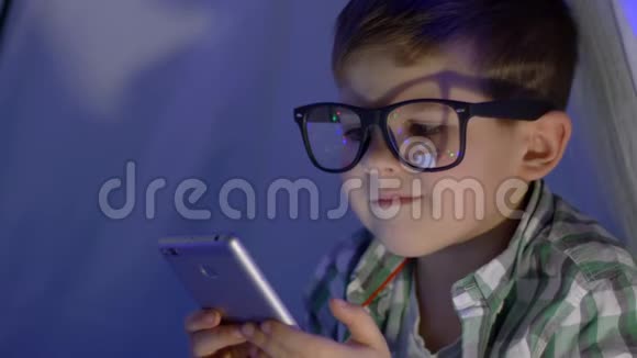 现代儿童戴眼镜的肖像用wigwam特写镜头观看视频进入智能手机视频的预览图
