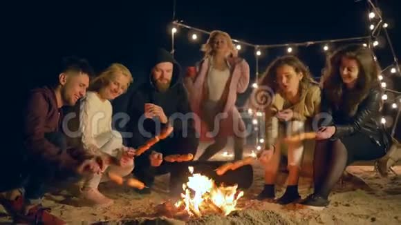 吃点火年轻人在篝火旁烤香肠晚上在户外放松视频的预览图