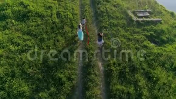 空中视频欢快的孩子和带着彩色丝带的少女在湖边散步视频的预览图