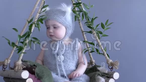 儿童服装穿松鼠套装的婴儿坐在绿色背景的藤蔓秋千上视频的预览图
