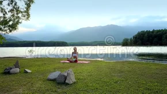女孩坐在湖边的石头前摆着莲花的姿势视频的预览图