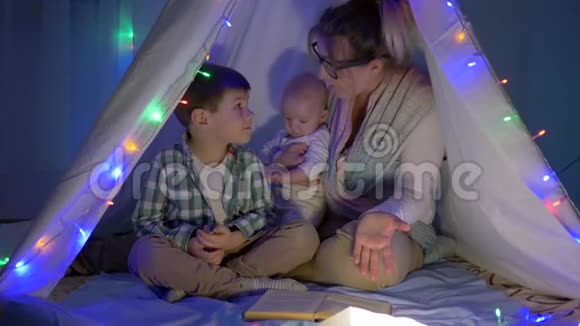 温馨的家妈妈正在为晚上躺在帐篷里的儿子读故事视频的预览图