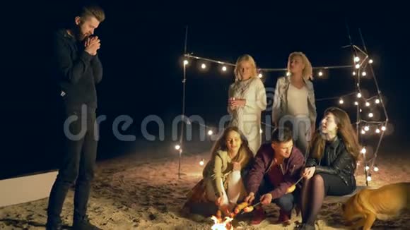 年轻人的游戏朋友们在假日里在沙滩上篝火旁玩有趣的娱乐活动视频的预览图