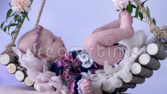小女孩躺在木制秋千上白色背景上装饰着鲜花视频的预览图