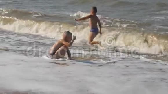宝贝在海滩上在海浪中两个男孩在金沙上玩冲浪头部覆盖的波浪视频的预览图