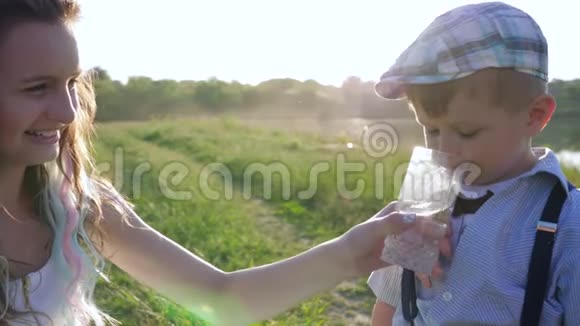 爱笑的少女在阳光下从杯子里给小男孩喝水视频的预览图