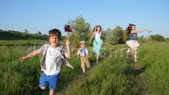 活跃的孩子们手里拿着五颜六色的风车和丝带在草坪上奔跑和欢笑视频的预览图
