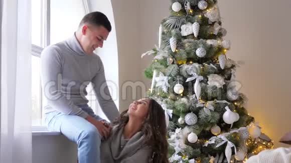 圣诞早晨头发上铺着人造雪的女孩在装饰好的圣诞树旁送礼物给丈夫视频的预览图