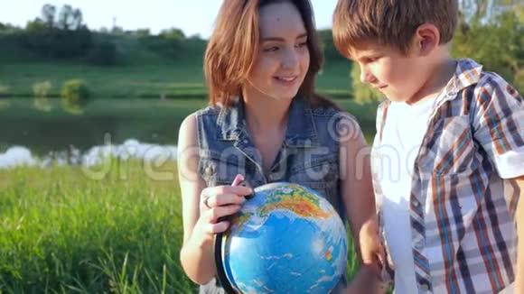 孩子们学习世界好奇的男孩和女孩青少年看地球的自然坐在河边的草地上视频的预览图