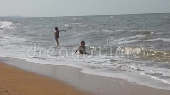 宝贝在海滩上在海浪中两个男孩在金沙上玩冲浪头部覆盖的波浪视频的预览图