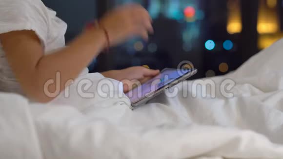 晚上坐在床上的小男孩特写镜头播放一台平板电脑电脑上有一座摩天大楼的轮廓视频的预览图