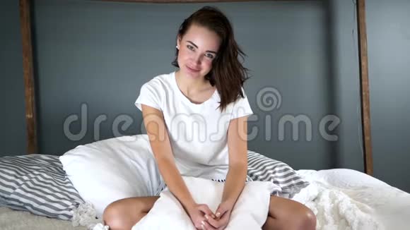 早晨年轻女子摇着头发坐在床上看着家里的摄像机视频的预览图