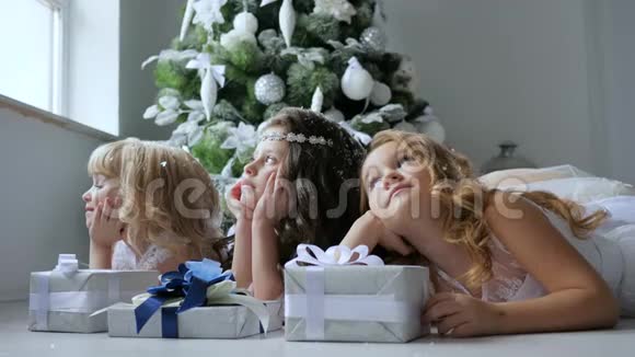 孩子们梦幻般地看着窗外的冬天窗外装饰着圣诞树地板上放着礼品盒视频的预览图